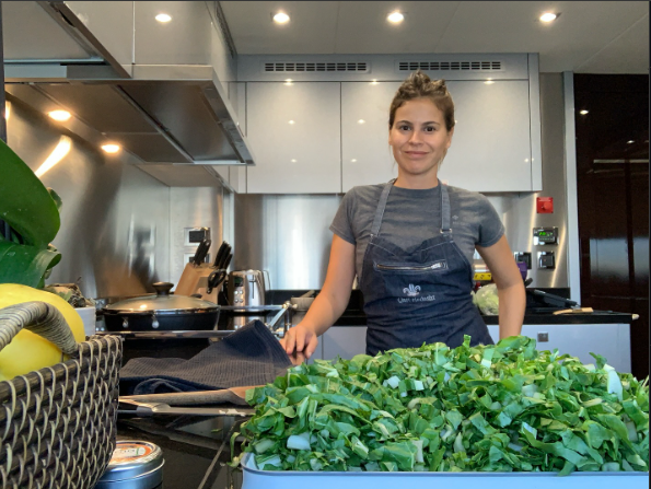 Ana Clelia en una cocina profesional junto a una bandeja de hojas verdes frescas